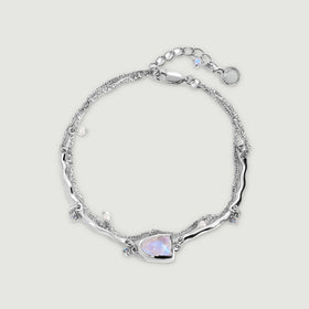 A sterling silver bracelet forms an oval with a raw moonstone, small pearls, blue charms, and an extender chain.
