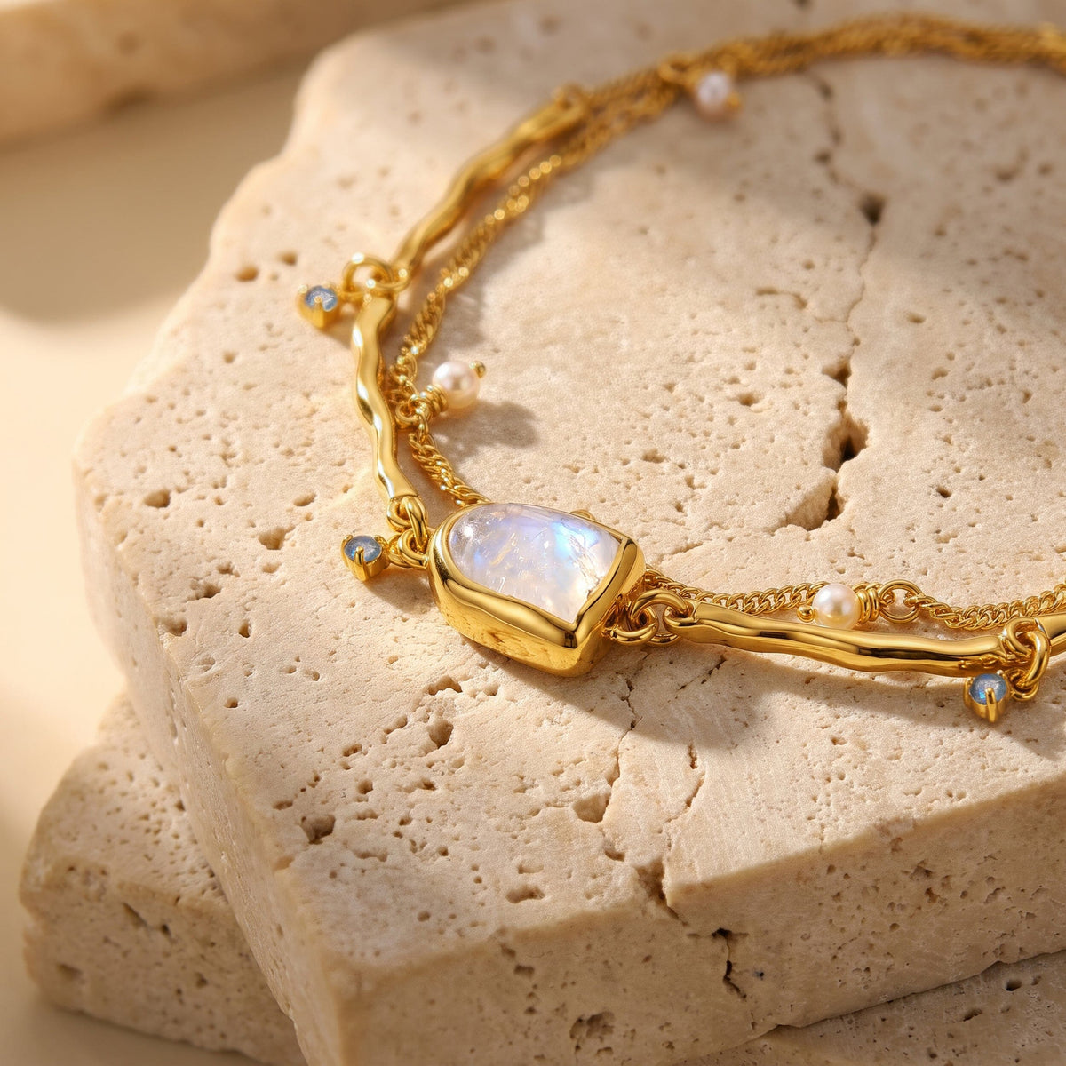 The gold vermeil bracelet rests on textured travertine with its moonstone setting, wavy links, and pearls in view.