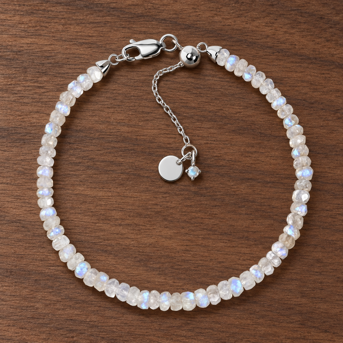 Lunar Tide rainbow moonstone beaded bracelet with sterling-silver clasp and extension chain on walnut wood.
