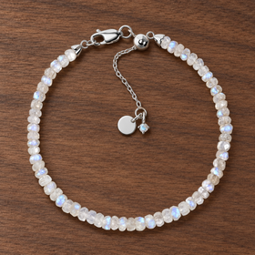 Lunar Tide rainbow moonstone beaded bracelet with sterling-silver clasp and extension chain on walnut wood.