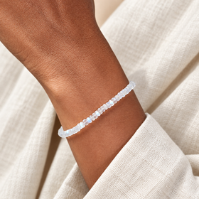 Close-up of the delicate white moonstone bead strand worn on a wrist beside ivory linen; one bracelet shown.