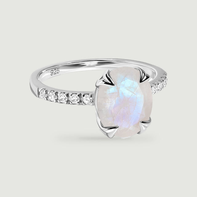 An oval moonstone with a blue sheen sits between clear shoulder stones on a polished silver ring.