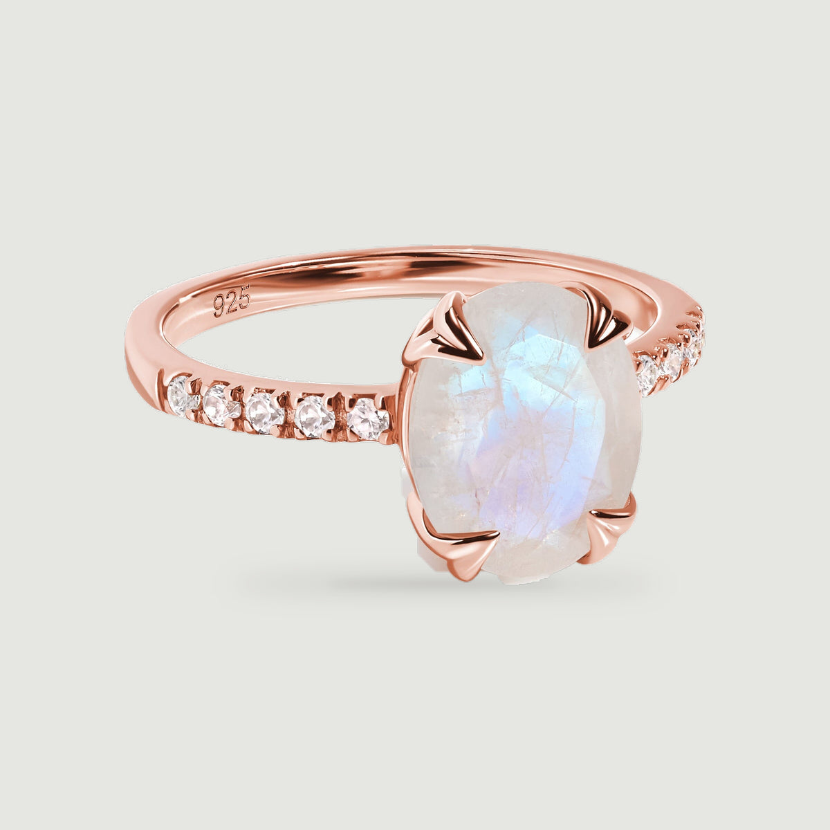 A rose gold vermeil ring displays an oval moonstone and rows of clear stones against a light gray background.