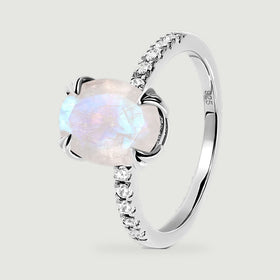 The angled silver ring shows the raised moonstone setting, curved band, and clear stones along its shoulders.
