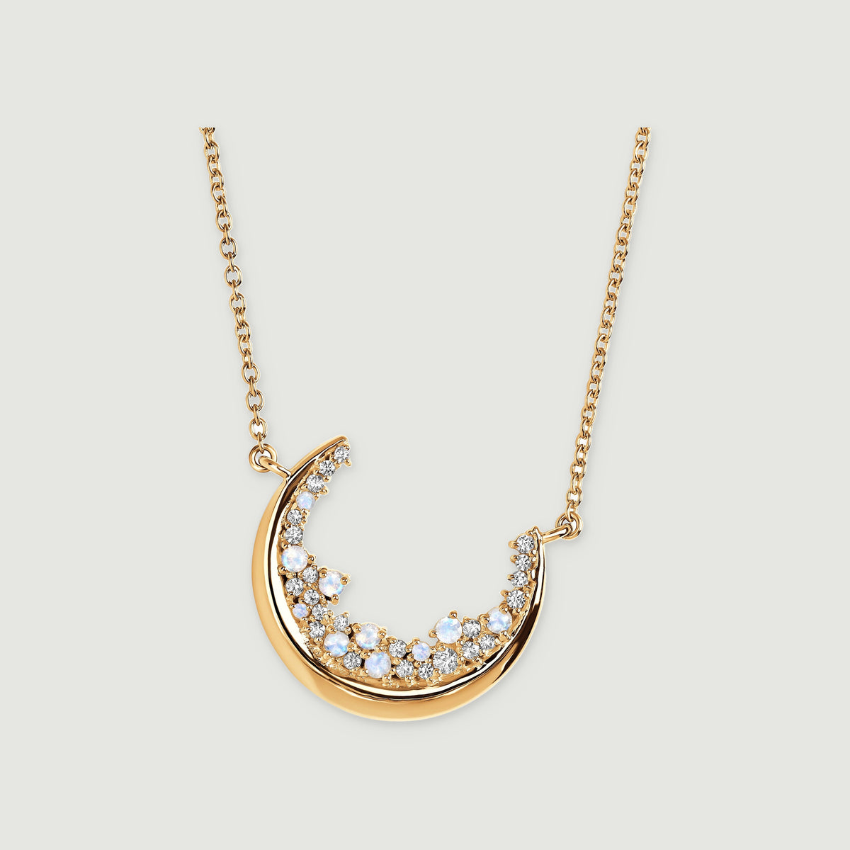 A yellow gold crescent pendant holds blue-white round stones and clear gems on a fine chain against light grey.