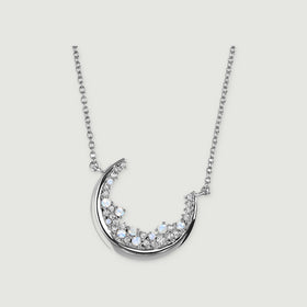 A silver crescent necklace with pale blue stones and clear gems is centered on a light grey surface.