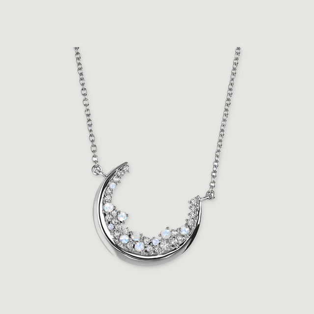 A silver crescent necklace with pale blue stones and clear gems is centered on a light grey surface.
