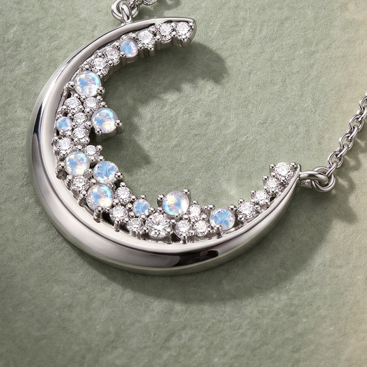 An angled close view reveals the polished silver crescent edge, raised stone settings, and chain attachment.