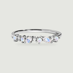 A white gold ring is centered on a light gray surface with a row of blue flashing moonstones and clear diamonds.