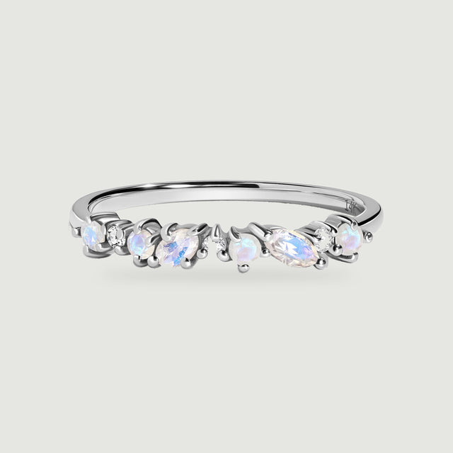 A white gold ring is centered on a light gray surface with a row of blue flashing moonstones and clear diamonds.