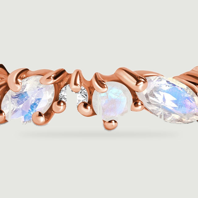 A close view shows oval and round moonstones secured by rose gold prongs around a small clear diamond.