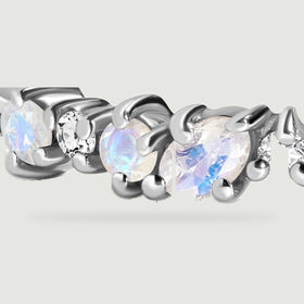 White gold prongs surround a blue flashing oval moonstone beside round stones and a clear diamond.