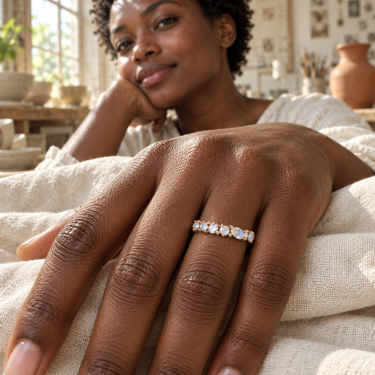 A rose gold moonstone and diamond ring is worn on a hand resting on ivory linen in a pottery studio.