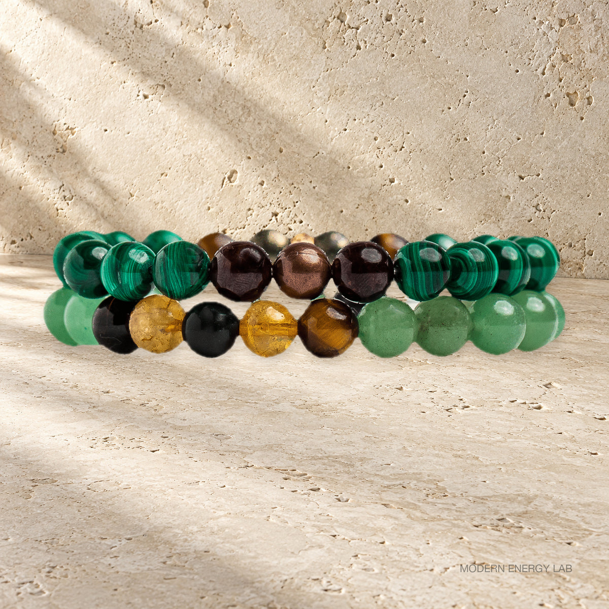 Side view of two malachite and citrine bead bracelets on warm travertine.
