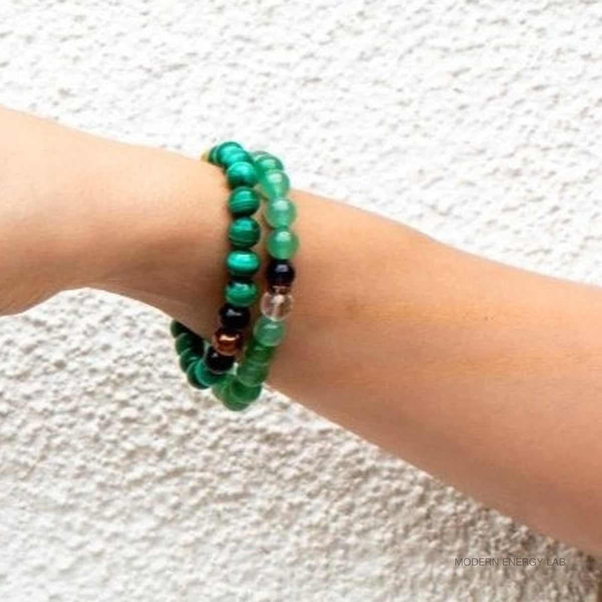 Two malachite and citrine bead bracelets worn on a wrist beside a textured wall.