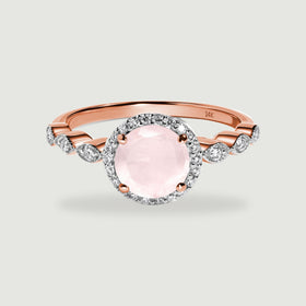A rose gold ring has a round pale pink stone, a diamond halo, and diamond-set shoulders on a light gray surface.