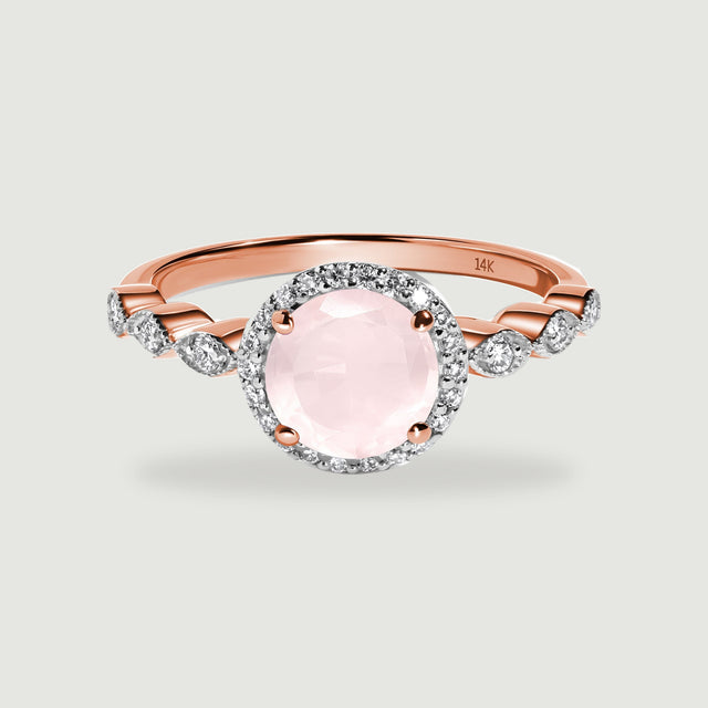 A rose gold ring has a round pale pink stone, a diamond halo, and diamond-set shoulders on a light gray surface.