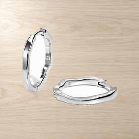 Pair of sculpted oval hoop earrings with gently wavy edges displayed on a light wood surface.