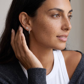 Side profile of a freckled woman touching a wavy hoop earring beneath a tiny round stud.