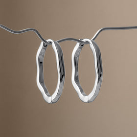 Pair of wavy oval hoops hanging from a curved chain against a warm taupe background.