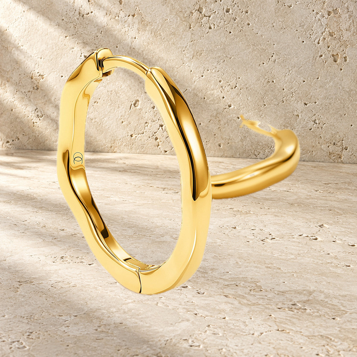 Pair of polished wavy hoops displayed against a textured stone backdrop with one earring in front.