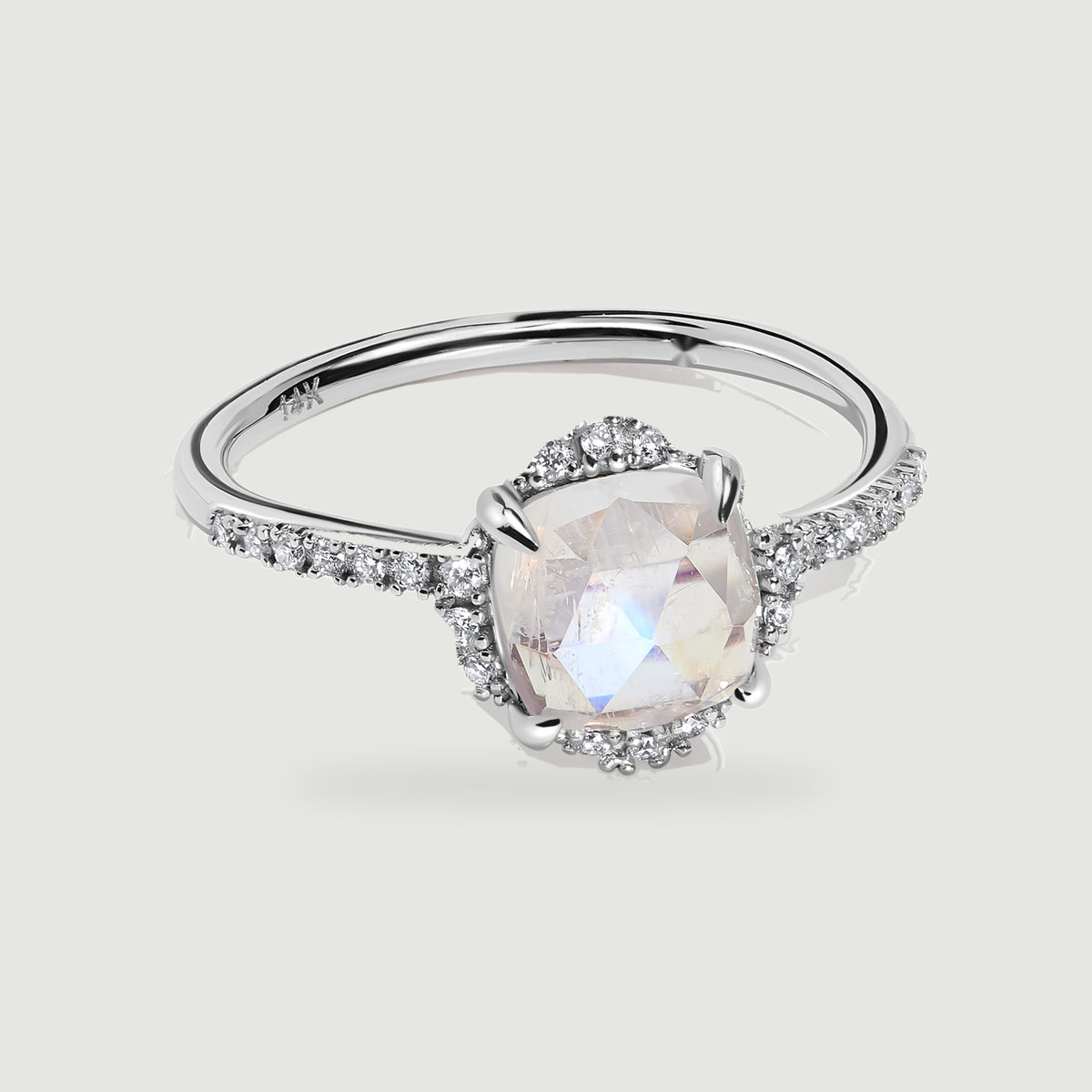 A white gold ring displays a faceted moonstone, four polished prongs, and diamond-set shoulders.