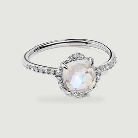 A white gold ring displays a faceted moonstone, four polished prongs, and diamond-set shoulders.