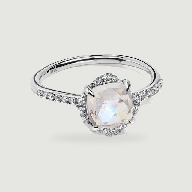 A white gold ring displays a faceted moonstone, four polished prongs, and diamond-set shoulders.