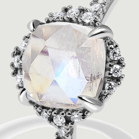 A tight angled view reveals the white gold setting, pale blue moonstone facets, and surrounding diamonds.