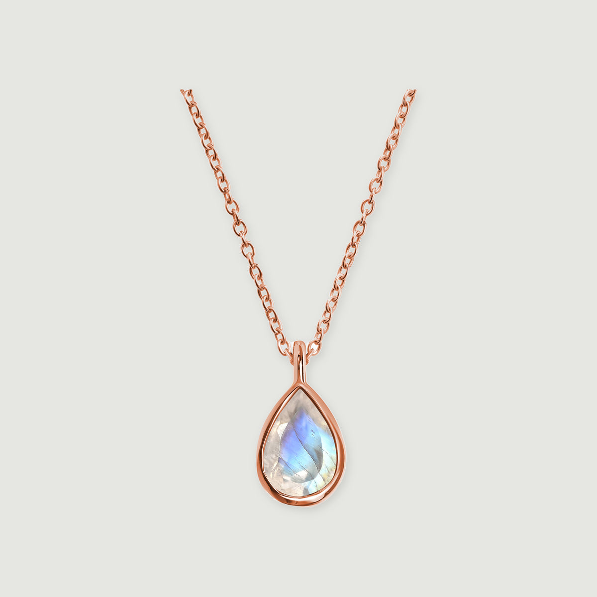 A rose gold necklace with a teardrop moonstone and a slim connecting bail rests against a light gray background.
