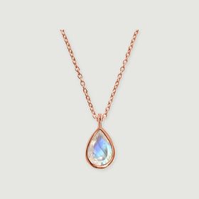 A rose gold necklace with a teardrop moonstone and a slim connecting bail rests against a light gray background.