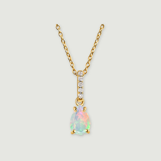 A yellow gold necklace has a pear-shaped opal pendant and five clear stones along the bail on a light grey background.
