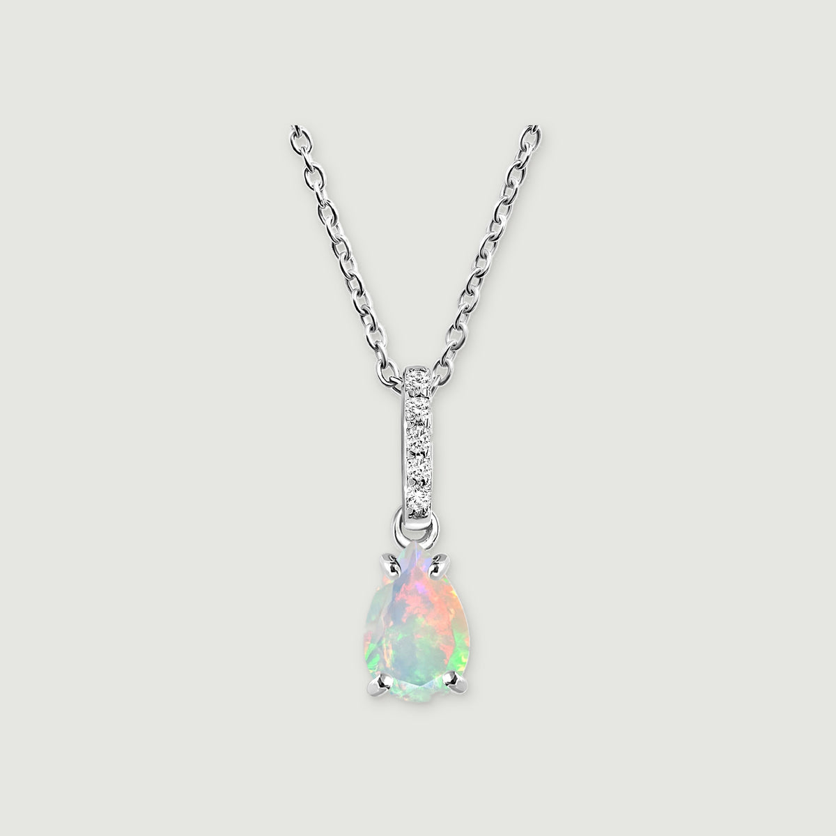A silver chain meets a stone-set bail above a pear-shaped opal pendant on a softly shadowed grey surface.