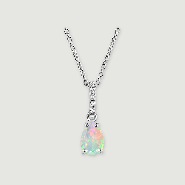A silver chain meets a stone-set bail above a pear-shaped opal pendant on a softly shadowed grey surface.