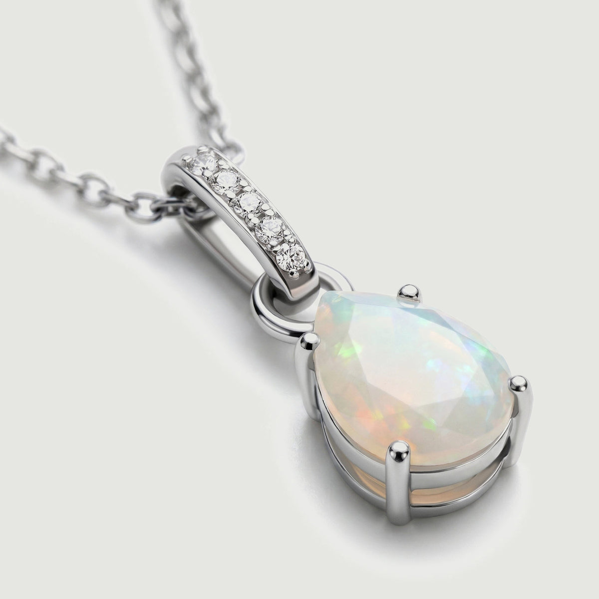 The silver pendant is shown at an angle with pale opal facets and a row of clear stones above it.