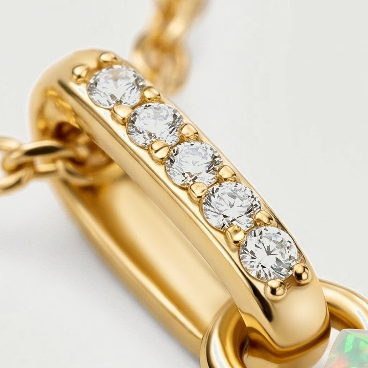 Five round clear stones sit along a polished yellow gold bail beside the connecting ring and the edge of the opal.
