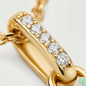Five round clear stones sit along a polished yellow gold bail beside the connecting ring and the edge of the opal.