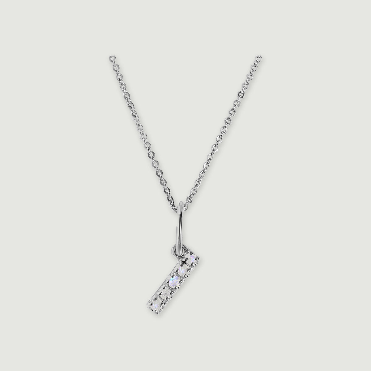 A silver chain holds a stone-set letter I pendant against a light gray background.