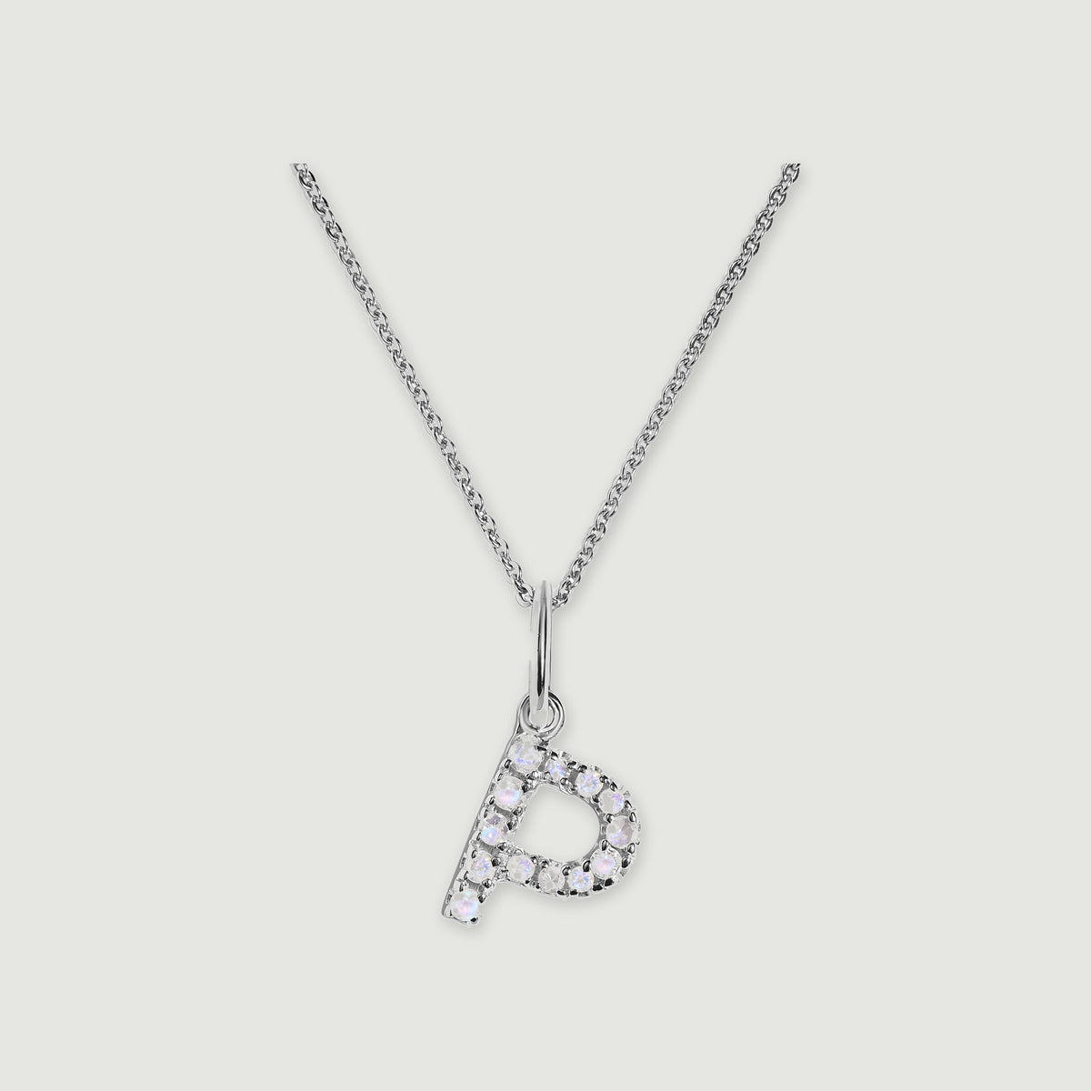 A silver chain holds a stone-set letter P pendant against a light gray background.
