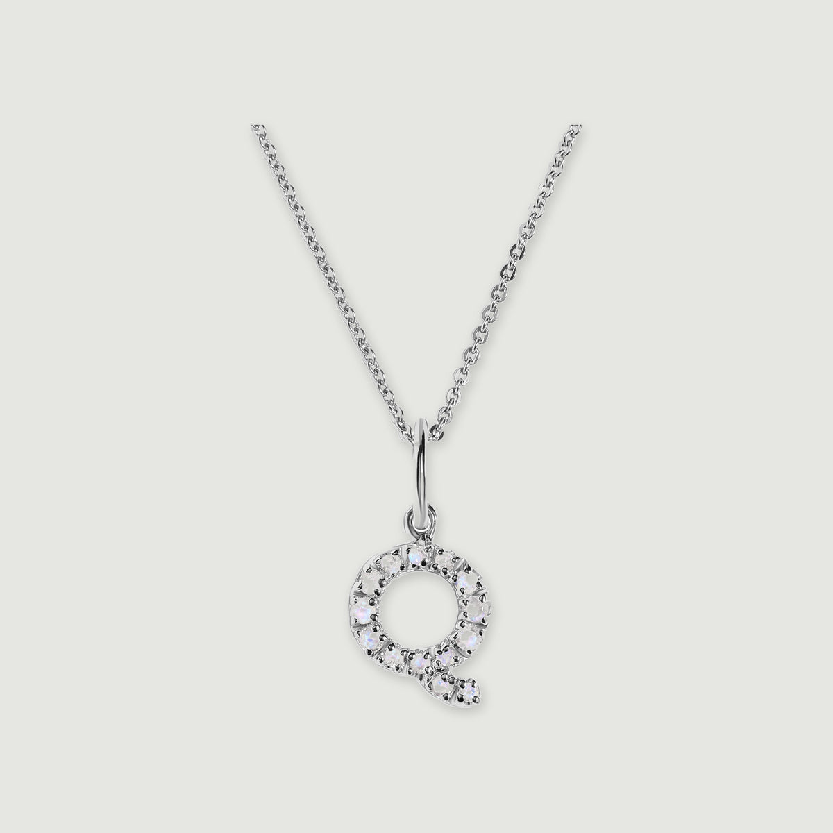 A silver chain holds a stone-set letter Q pendant against a light gray background.