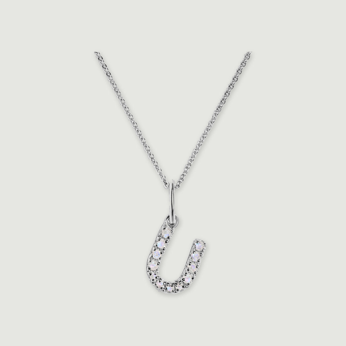 A silver chain holds a stone-set letter U pendant against a light gray background.