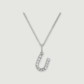 A silver chain holds a stone-set letter U pendant against a light gray background.
