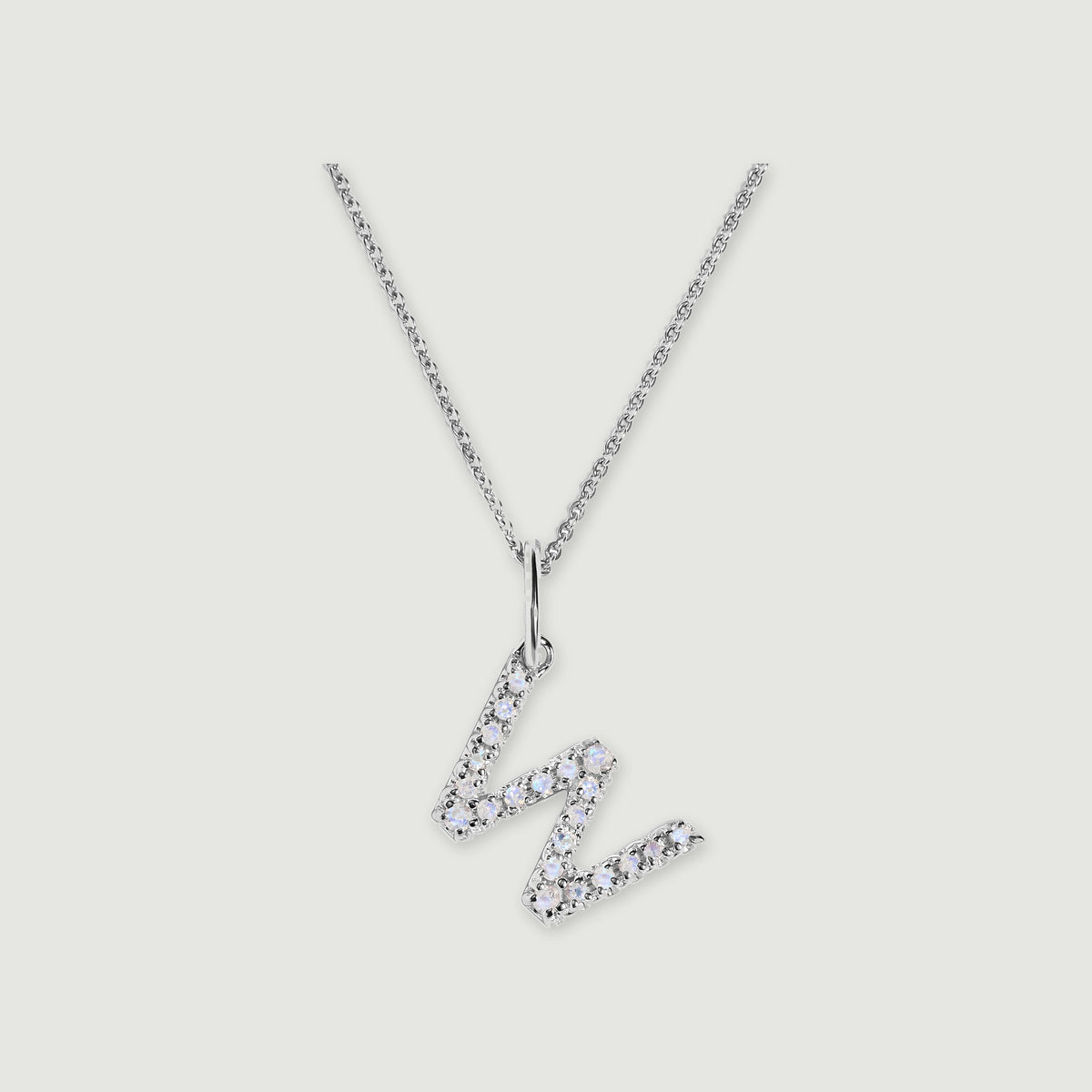 A silver chain holds a stone-set letter W pendant against a light gray background.