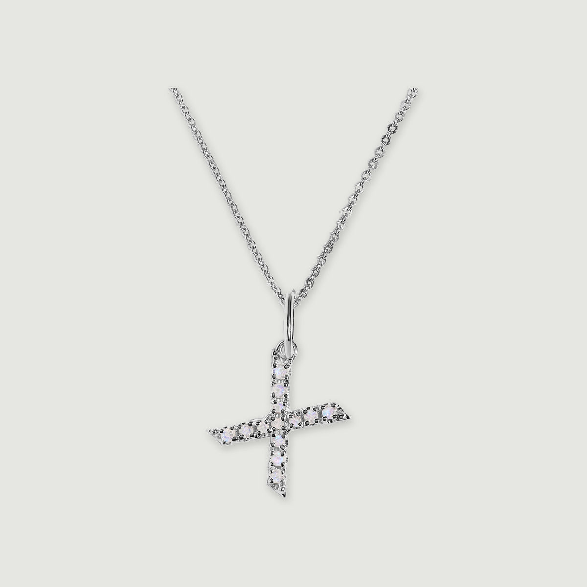 A silver chain holds a stone-set letter X pendant against a light gray background.