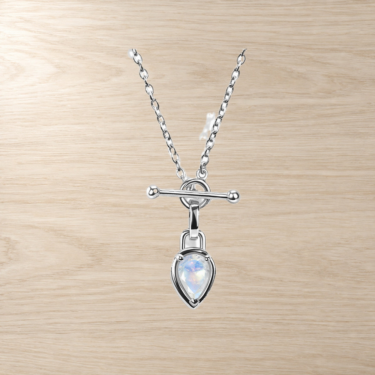 Necklace on a pale wood surface, featuring a round toggle bar and pear-shaped iridescent moonstone pendant.