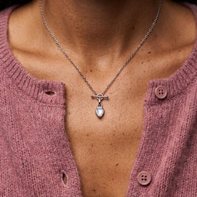 Close-up of a person wearing a delicate chain necklace with a toggle bar and glowing pear-shaped pendant.