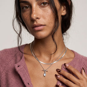 Portrait of a freckled person wearing the pear-shaped moonstone pendant layered with another necklace.