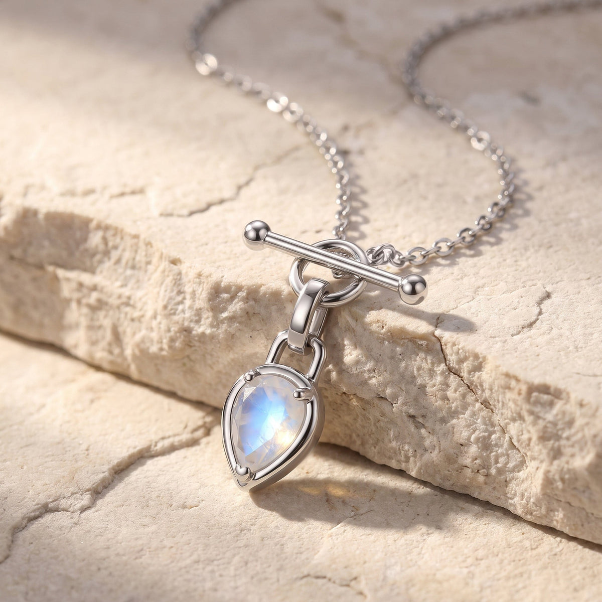 Pear-shaped moonstone toggle necklace arranged across a pale textured stone surface in soft sunlight.