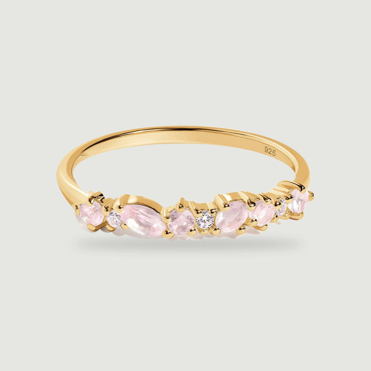 A yellow gold ring with pale pink rose quartz and small clear stones rests on a light gray surface.