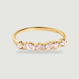 A yellow gold ring with pale pink rose quartz and small clear stones rests on a light gray surface.